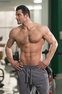 Shirtless muscular man with hands on hip standing in gym