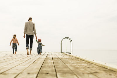 Full length rear view of family walking on pier at sea against clear sky