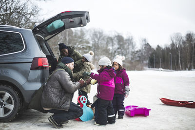 Man helping daughter by family unloading car trunk during winter