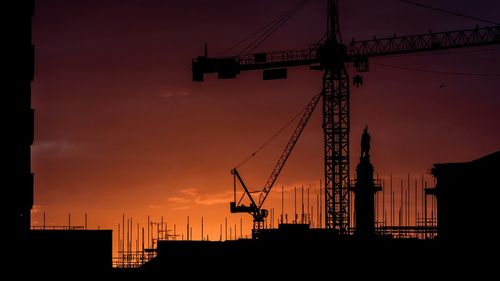 Low angle view of silhouette cranes at sunset