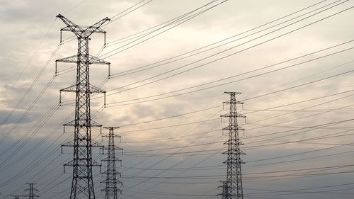 Low angle view of electricity pylon against sky during sunset