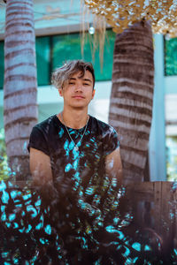 Portrait of young man looking at camera, sitting against palms.