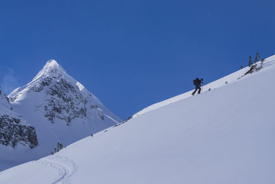 Low angle view of man climbing on snow covered mountain against blue sky