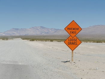 Sign board on dirt road against mountain