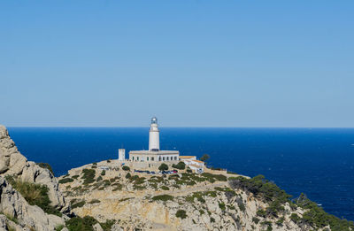 Lighthouse by sea against clear blue sky