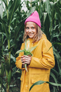 Stylish teenage girl in yellow raincoat and hot pink hat laughing on corn field