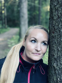 Portrait of smiling young woman against tree trunk