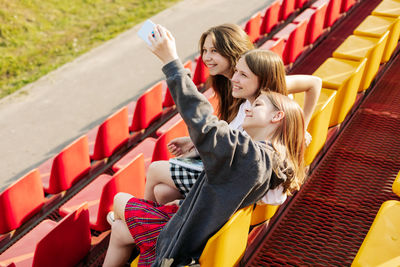 Three charming friends take selfies on their phone at the school stadium. the concept of friendship.