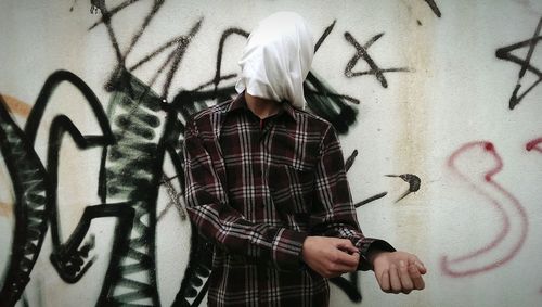 Man with face covered by cloth against graffiti wall
