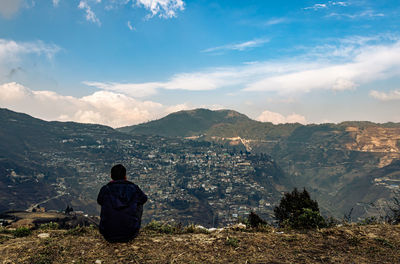 Rear view of man looking at mountains against sky