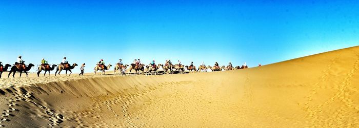 People on sand against clear blue sky