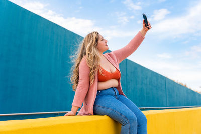 Young woman taking selfie against wall