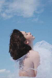 Low angle view of young woman in white dress against sky