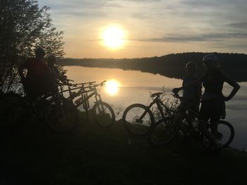 Silhouette people riding bicycle against sky during sunset