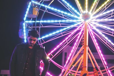 Young man standing against illuminated ferris wheel at night