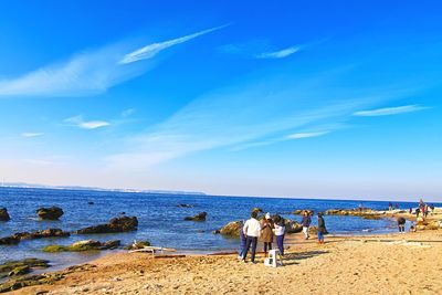 People standing on beach against blue sky