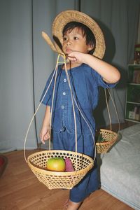 Cute boy carrying fruits in basket while standing on floor at home