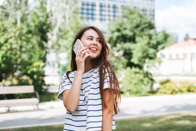 Portrait of young woman student with long hair using mobile phone in city park