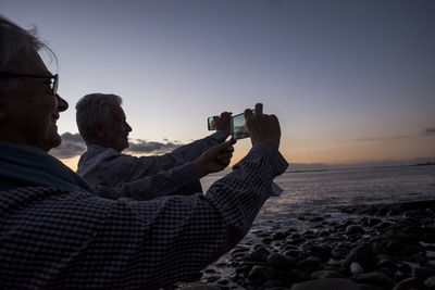 Couple taking selfie from mobile phones at beach during sunset