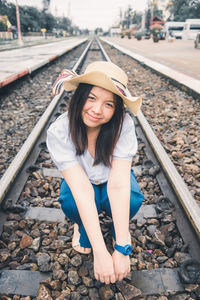 Portrait of woman sitting on railroad track against sky