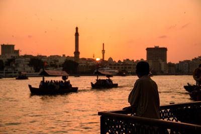 Rear view of silhouette people on building against sky during sunset