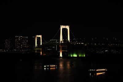 Illuminated city by river against sky at night