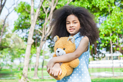 Portrait of girl holding toy against trees