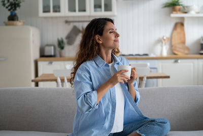 Young woman using phone while sitting on sofa at home