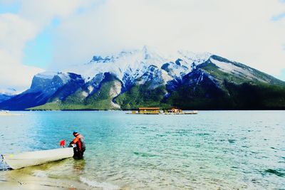 Side view of man with boat in lake against cloudy sky