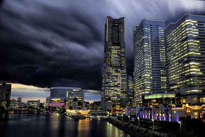 Illuminated buildings by river against sky in city at night