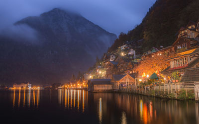 Illuminated buildings by river against sky at night