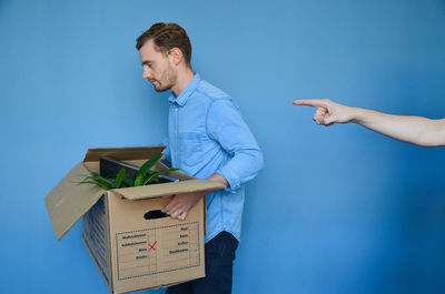 Hand pointing at young man carrying cardboard box after getting fired