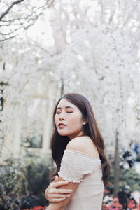 Side view of young woman with eyes closed standing against plants in park