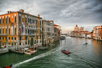 Boats in canal by buildings against sky during sunset