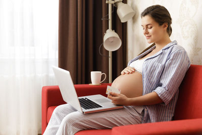 Pregnant woman with laptop sitting on sofa at home