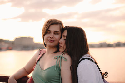 Portrait of happy lesbian couple standing on bridge at sunset