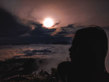 Rear view of woman looking at sea against sunset sky