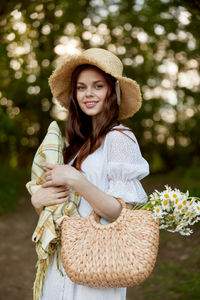 Portrait of young woman wearing hat standing against trees