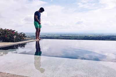 Side view of man standing at poolside against sky