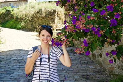 Portrait of happy woman holding purple flowers while standing on footpath
