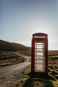 Telephone booth by road against clear sky