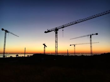 Silhouette cranes against sky during sunset