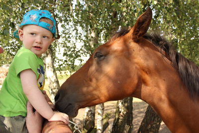Frightened boy standing in front of horse against trees