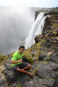 Portrait of man sitting by waterfall