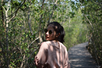 Young woman wearing sunglasses standing by plants on street