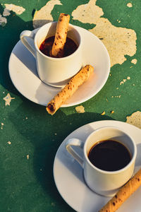 Cups of espresso coffee with rolled wafer cookies on green peeling paint concrete table