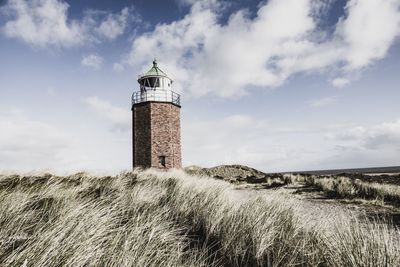 Lighthouse on field by building against sky