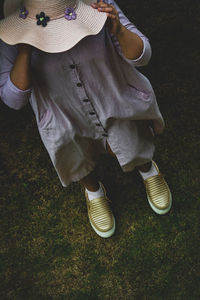 A girl wearing a dress and a hat standing on the grass while the wind is blowing 