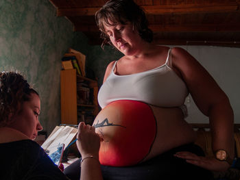 Woman painting on pregnant friend belly