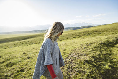 Side view of woman walking on grassy field against sky